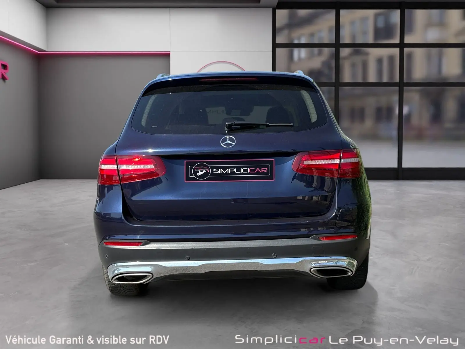 Vue arrière d'un Mercedes GLC 350 E HYBRID FASCINATION 4MATIC bleu avec feux allumés et double sortie d'échappement chromée.