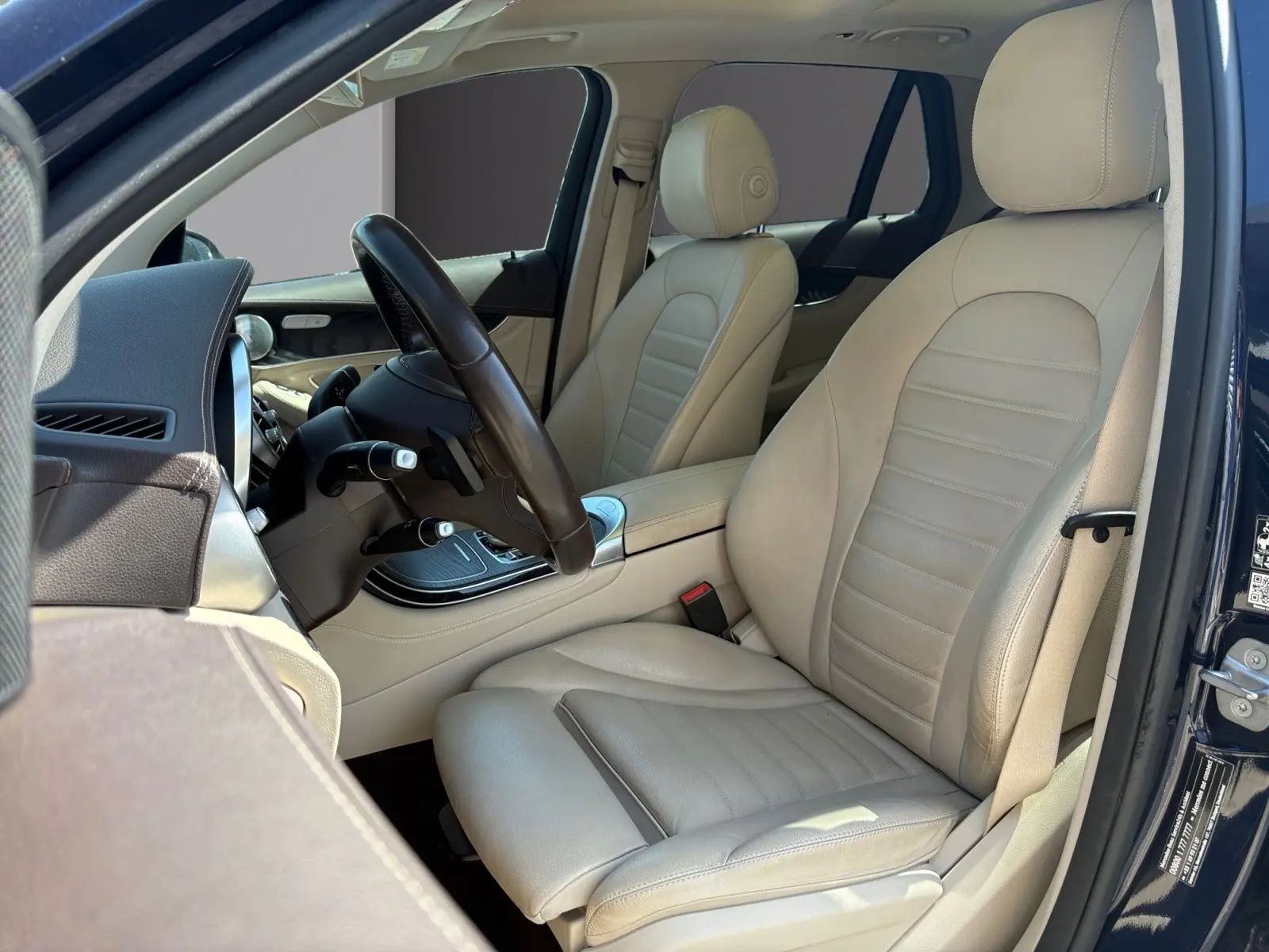 Vue intérieure côté conducteur d’un Mercedes GLC 350 E Hybrid Fascination bleu, avec sellerie cuir beige et volant noir.