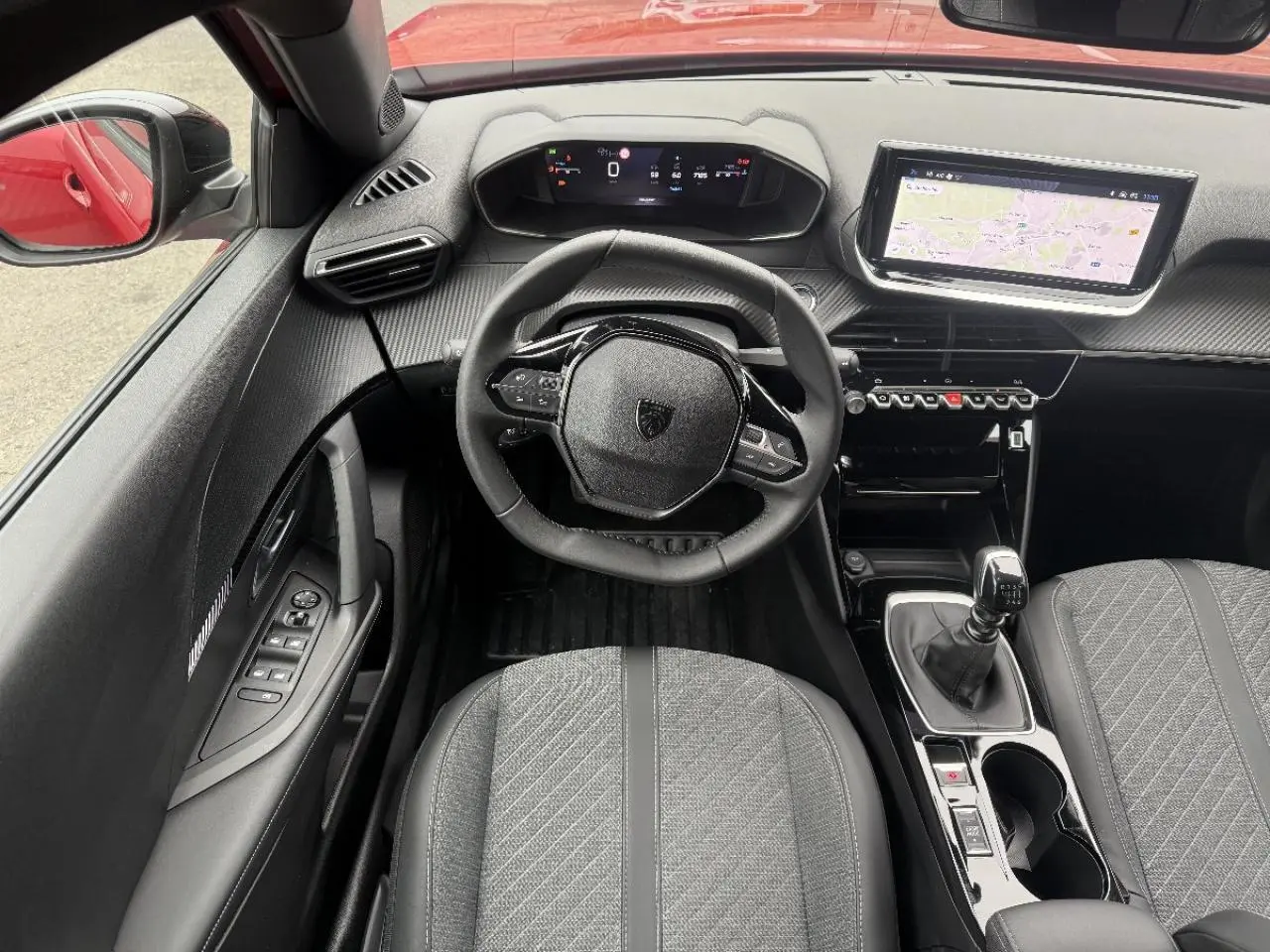 Vue intérieure centrée sur le volant et la console centrale d'une Peugeot 2008 rouge elexir, avec boîte manuelle et écran tactile.