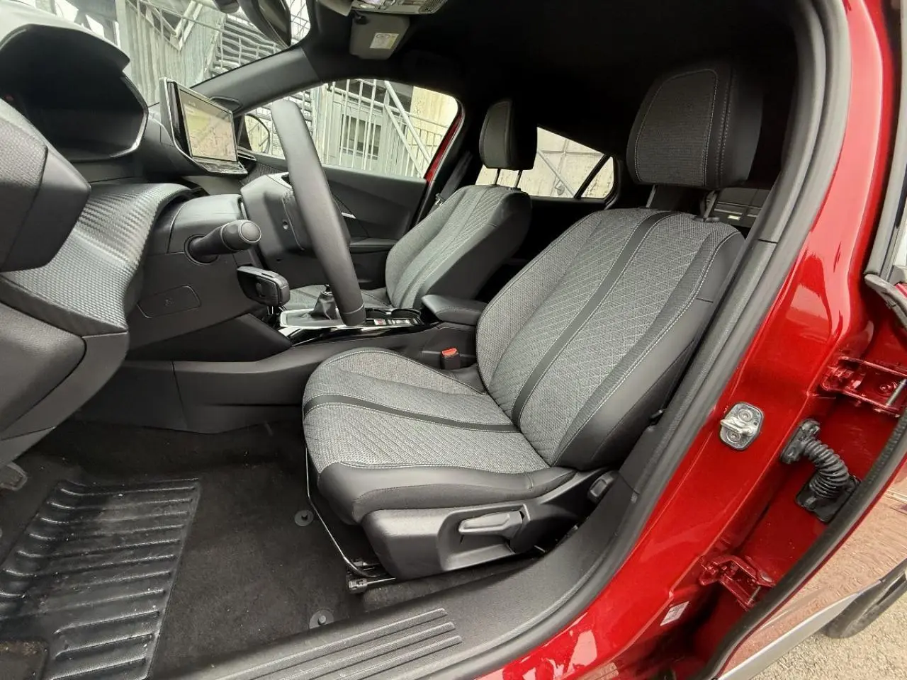 Vue intérieure côté conducteur du Peugeot 2008 rouge elixir 2025, sièges tissu gris et console centrale avec boîte manuelle.