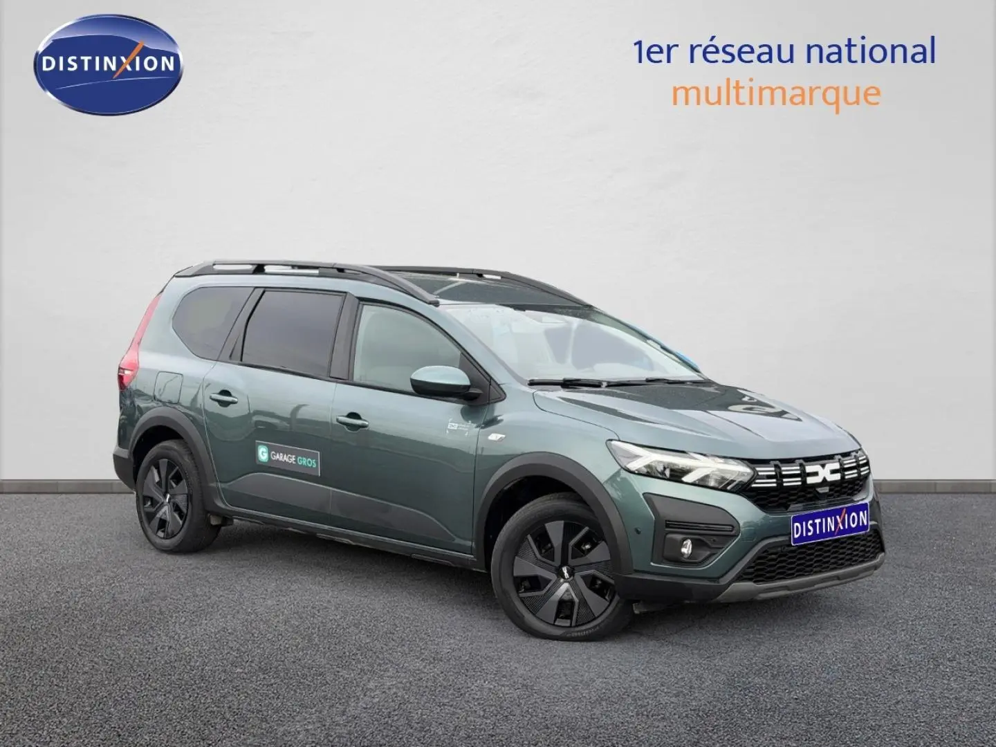 Dacia Jogger Vert Cèdre métallisé en vue 3/4 avant droit, avec barres de toit et vitres teintées.