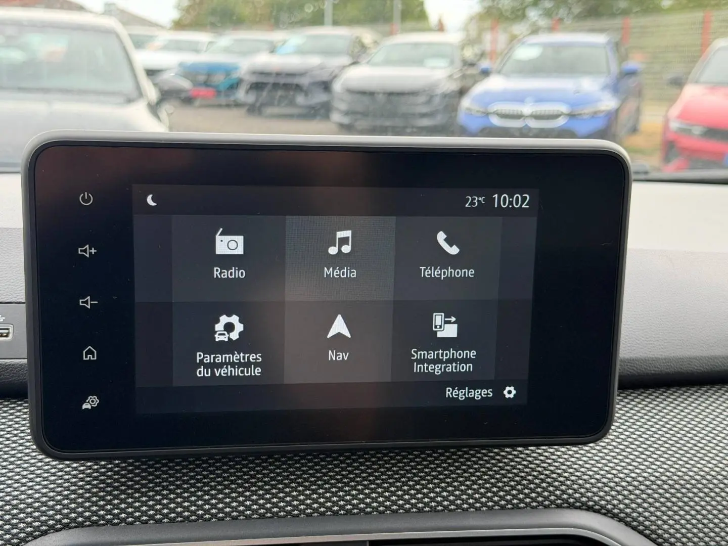 Écran tactile central du tableau de bord du Dacia Jogger avec vue floue sur plusieurs voitures en arrière-plan.