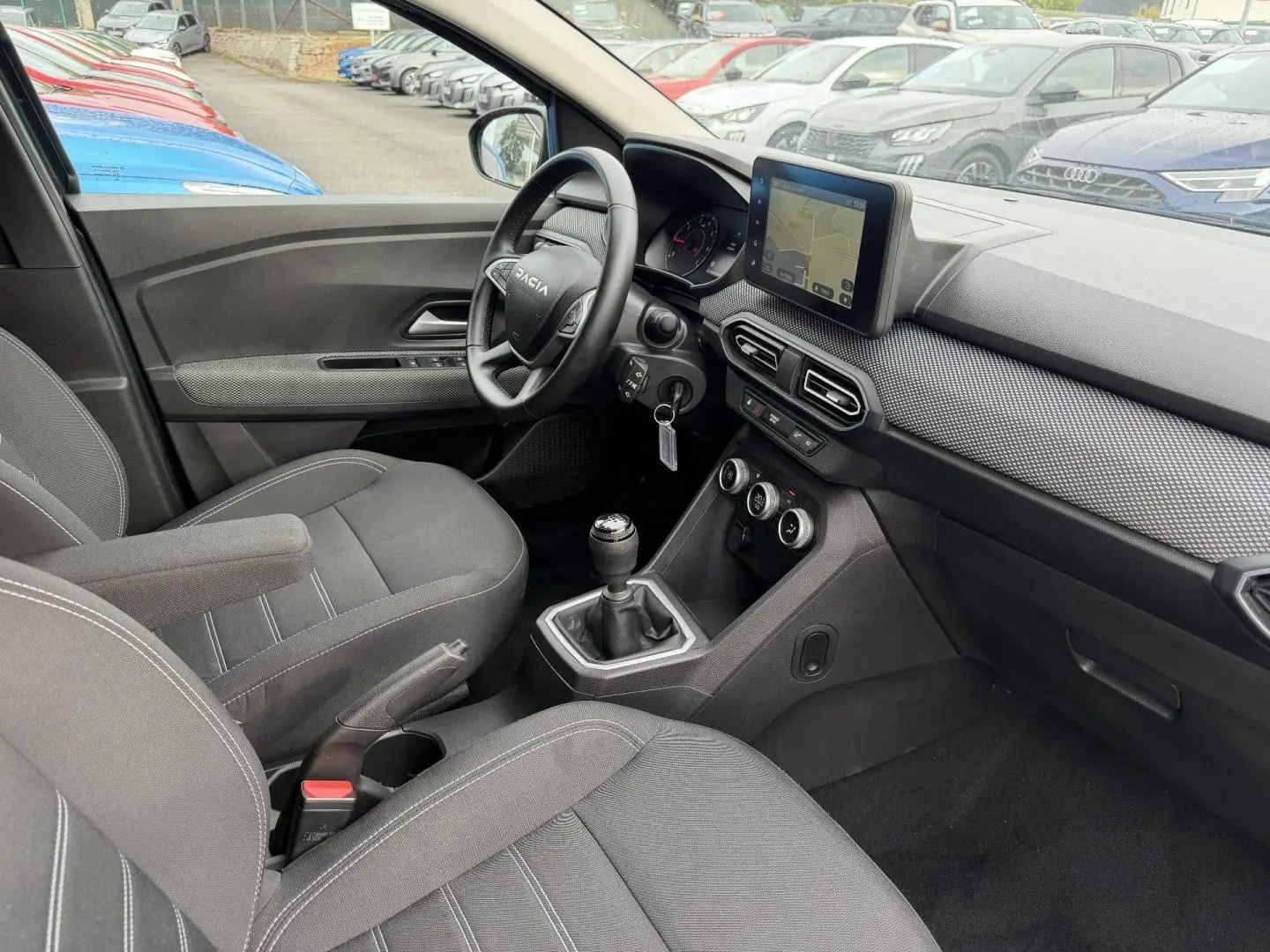 Intérieur avant droit du Dacia Jogger 2025, volant multifonctions, écran tactile et sièges tissu gris.