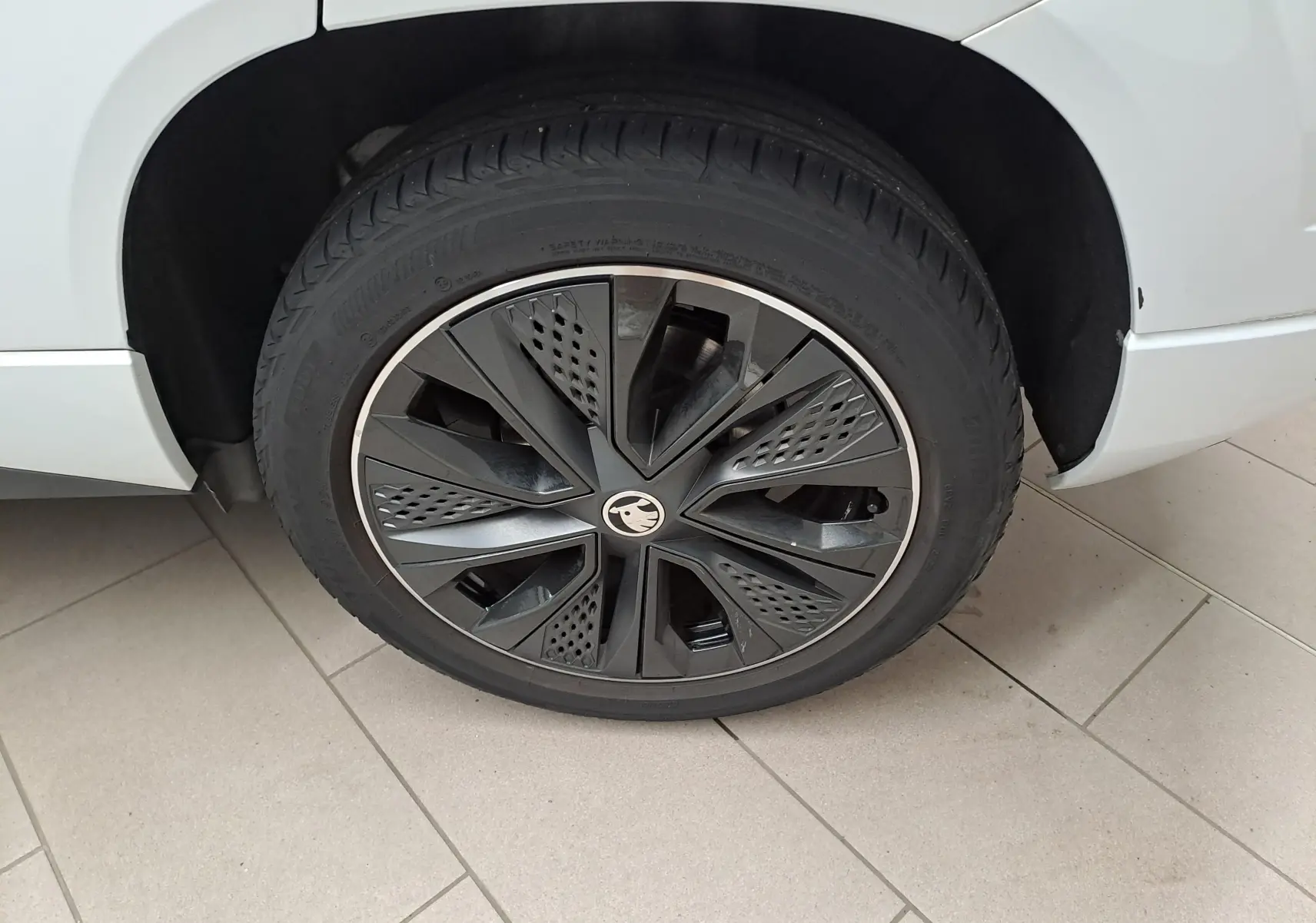 Gros plan sur la roue avant droite d’un Skoda Karoq blanc Lune, mettant en valeur la jante noire au design sportif.