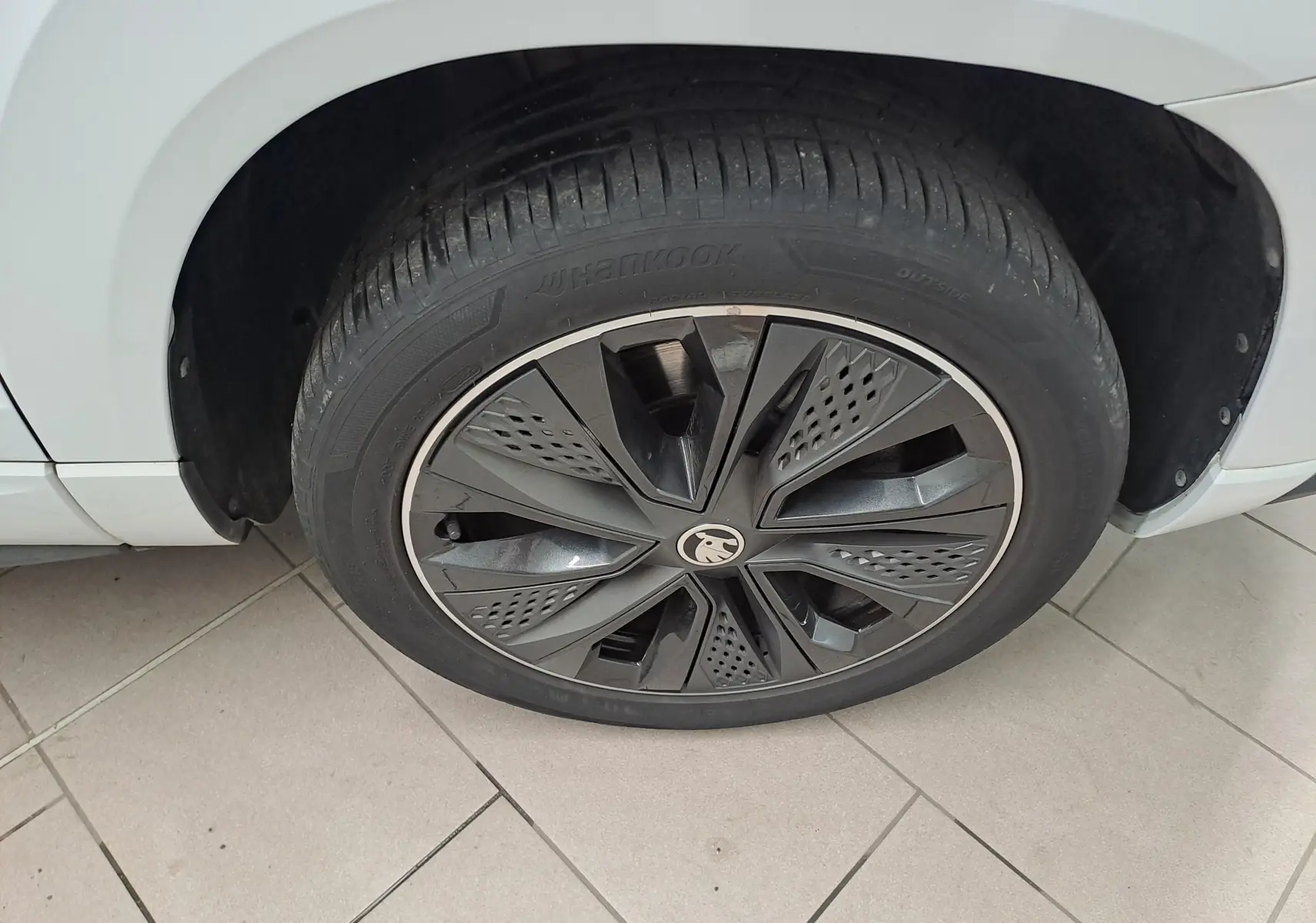 Gros plan sur la roue avant gauche d’un Skoda Karoq blanc Lune, mettant en valeur la jante noire et grise au design moderne.