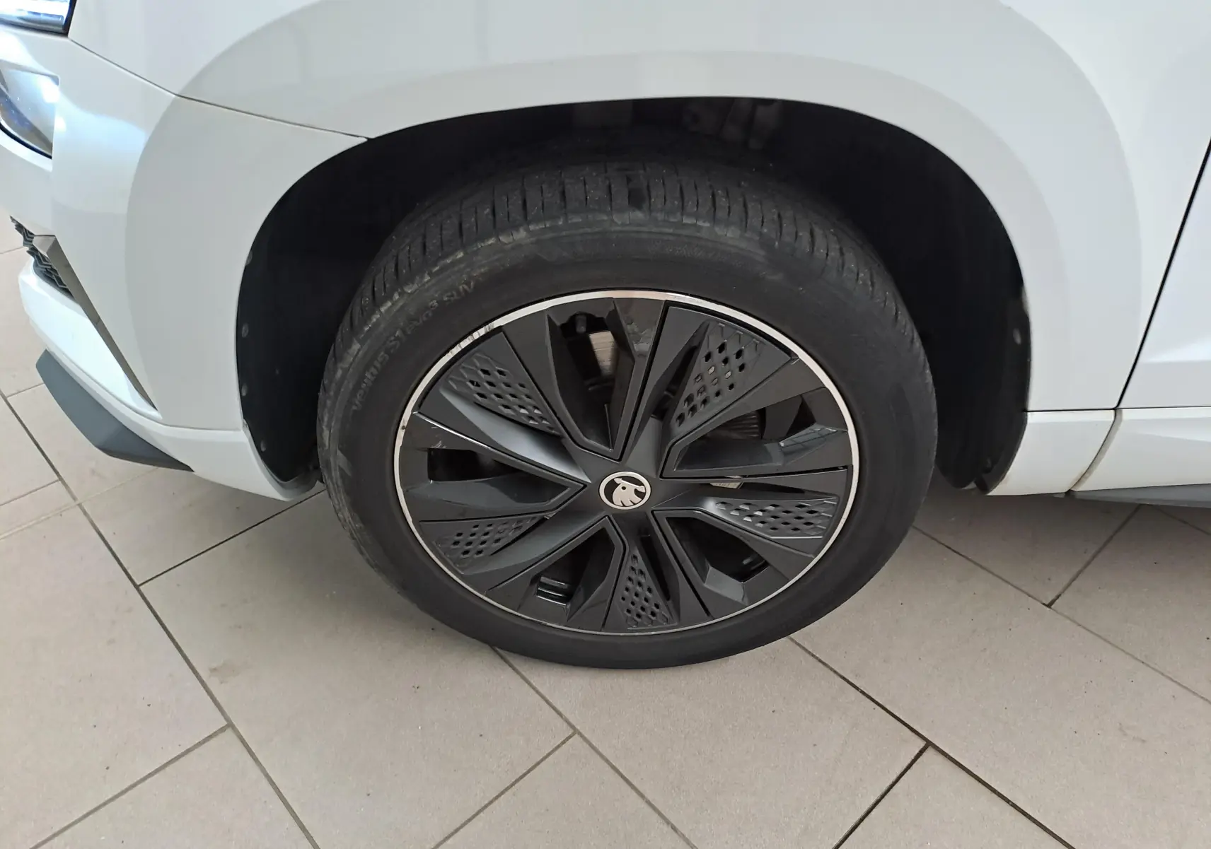 Gros plan sur la roue avant gauche du Skoda Karoq blanc Lune, mettant en valeur la jante noire au design moderne.