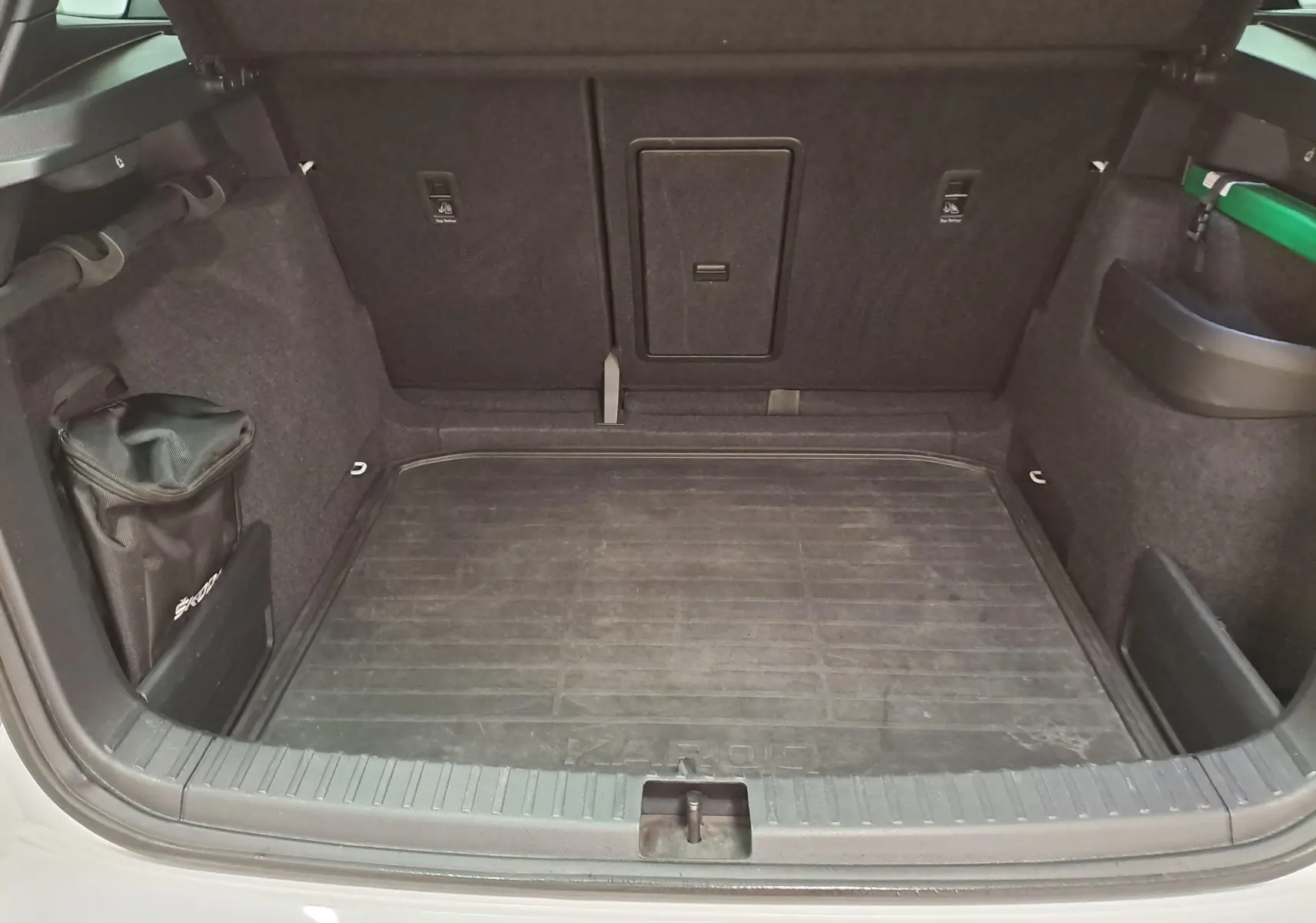 Coffre ouvert du Skoda Karoq blanc Lune 2022, vue intérieure montrant le tapis de sol et les rangements latéraux.