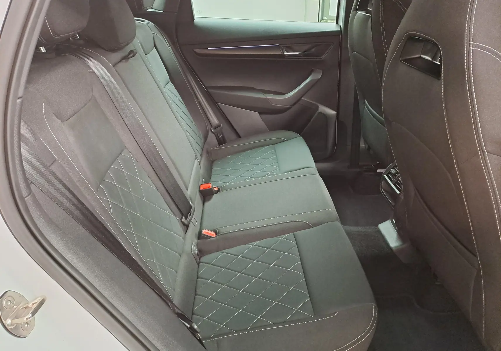 Vue intérieure côté gauche des sièges arrière en tissu noir avec surpiqûres blanches du Skoda Karoq 2022 Blanc Lune Sportline.