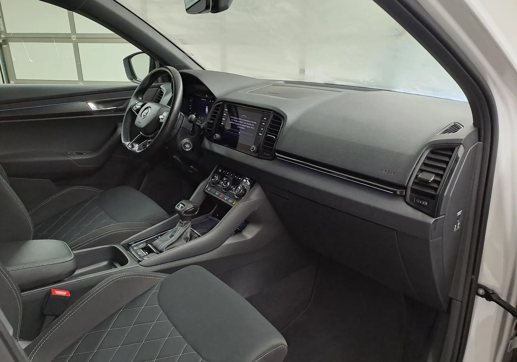Vue intérieure côté conducteur du Skoda Karoq 2022, avec sièges noirs matelassés et console centrale moderne.