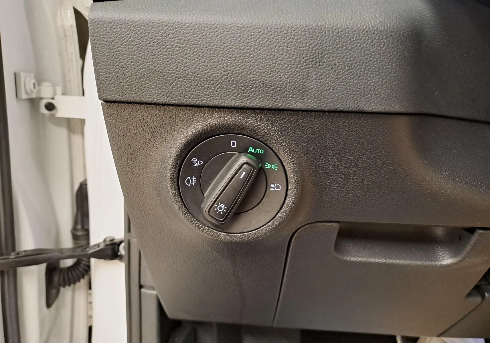 Gros plan sur le sélecteur de phares noir dans l'habitacle du Skoda Karoq Blanc Lune, côté gauche du tableau de bord.