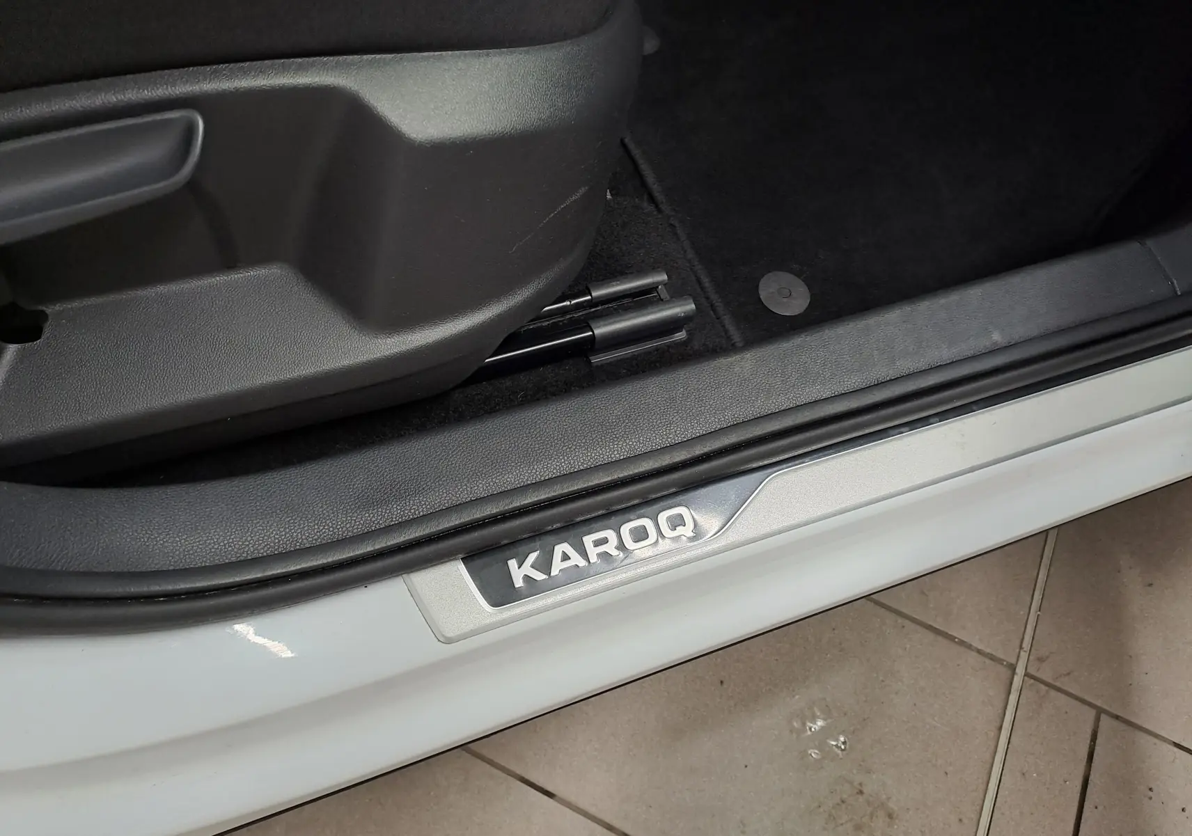 Gros plan sur la plaque de seuil de porte côté gauche du Skoda Karoq blanc lune, intérieur noir visible.