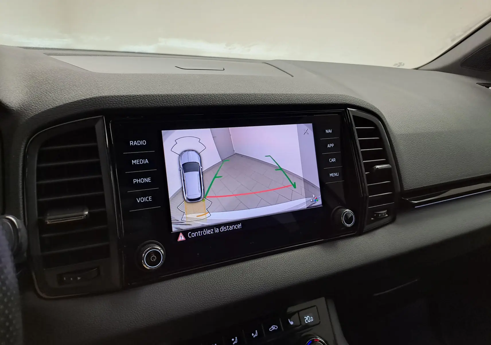 Écran central du tableau de bord montrant la caméra de recul du Skoda Karoq blanc, avec guidage de trajectoire en intérieur.