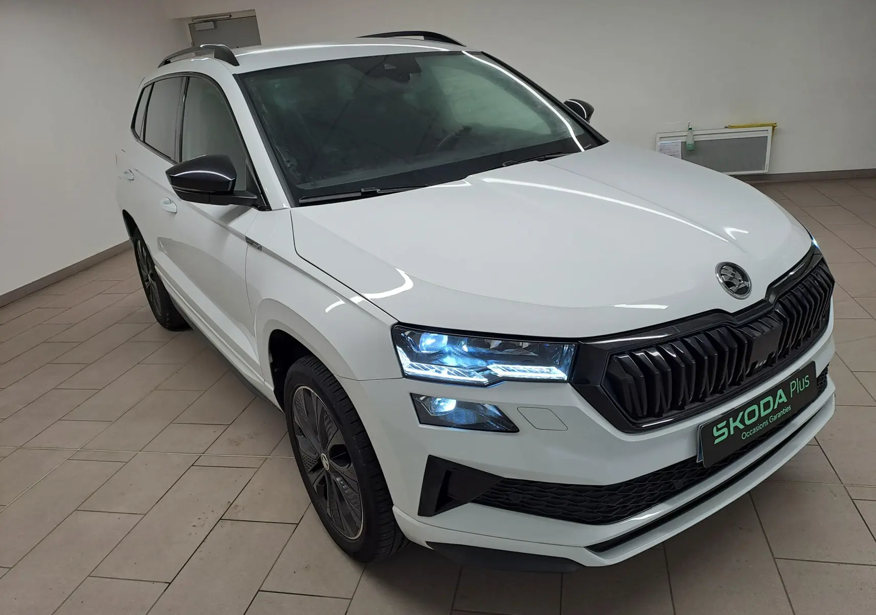 Vue 3/4 avant droite du Skoda Karoq blanc lune 2022 avec calandre noire et feux LED allumés en intérieur.