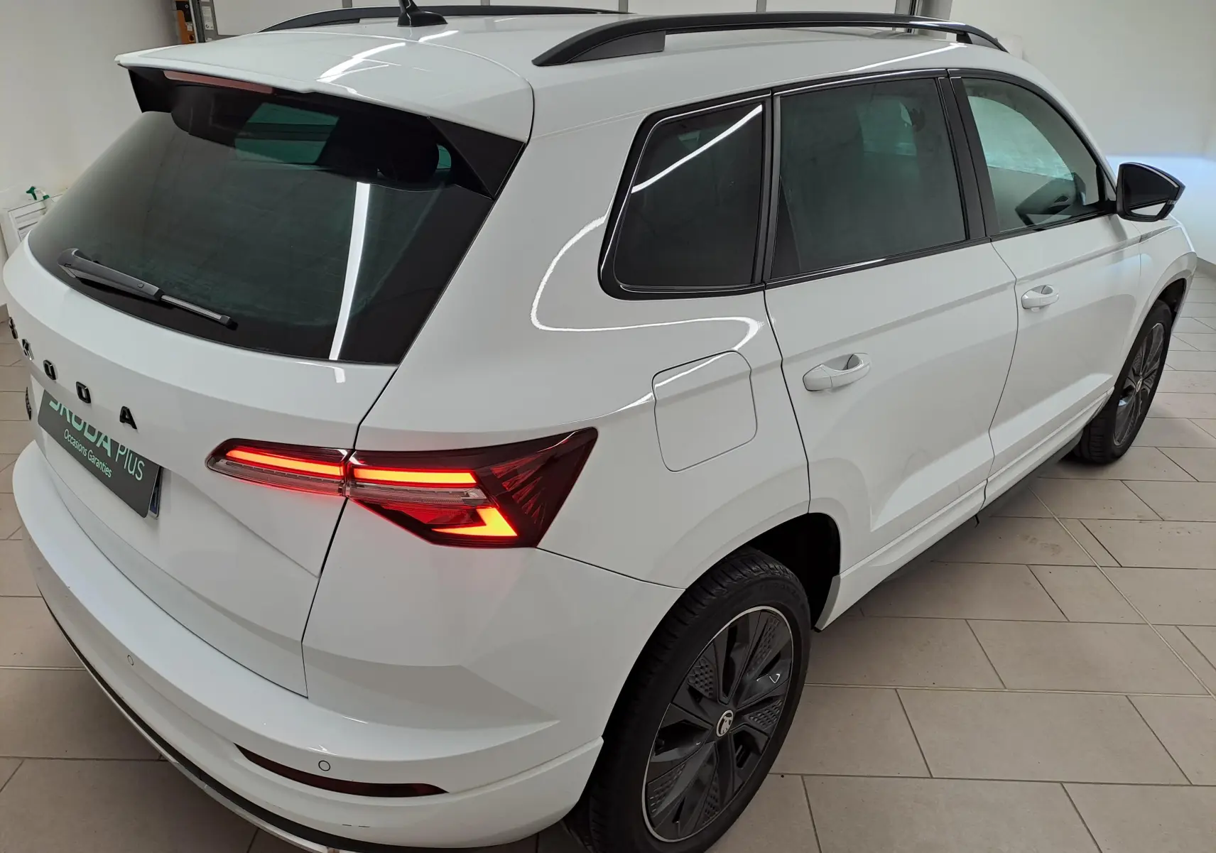 Vue 3/4 arrière droite du Skoda Karoq blanc lune 2022 avec feux arrière allumés et jantes noires distinctives.