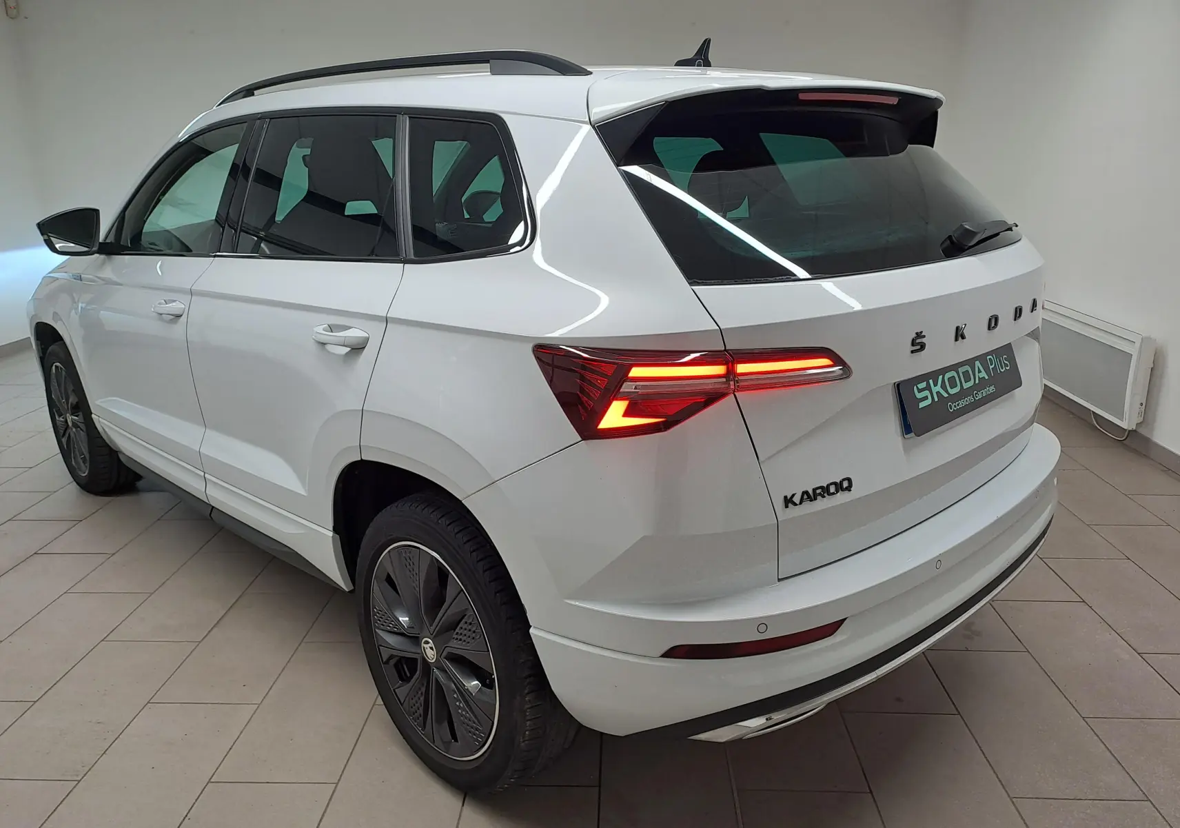 Vue 3/4 arrière droite du Skoda Karoq blanc lune 2022 avec feux allumés et jantes noires sportline.