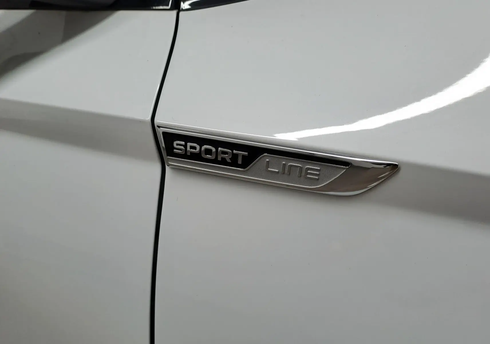 Gros plan sur l’inscription Sportline sur la portière blanche métallisée d’un Skoda Karoq 2022.