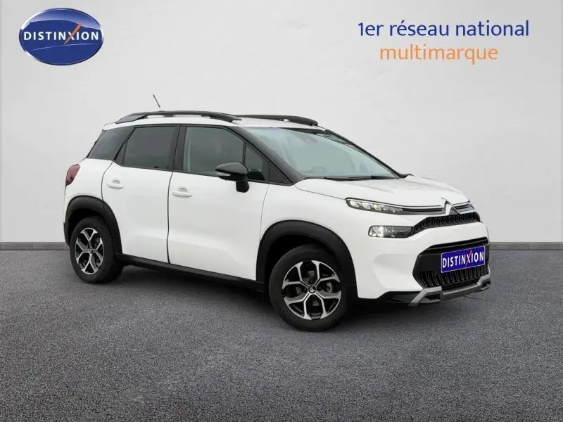 Vue 3/4 avant droit d'un Citroën C3 Aircross blanc Banquise avec barres de toit noires et jantes alliage.