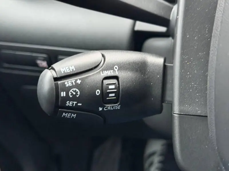 Gros plan sur la commande de régulateur de vitesse noire à gauche du volant dans une Citroën C3 Aircross blanc banquise 2024.