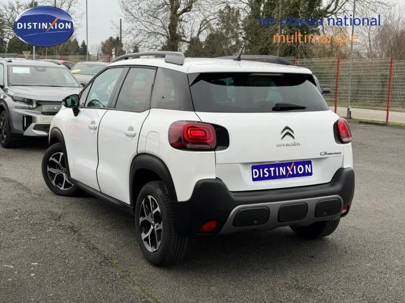 Vue 3/4 arrière droite d'un Citroën C3 Aircross blanc Banquise avec barres de toit et jantes alu noires.