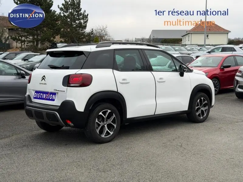 Vue 3/4 arrière droite d'un Citroën C3 Aircross blanc Banquise avec barres de toit et jantes alu noires.