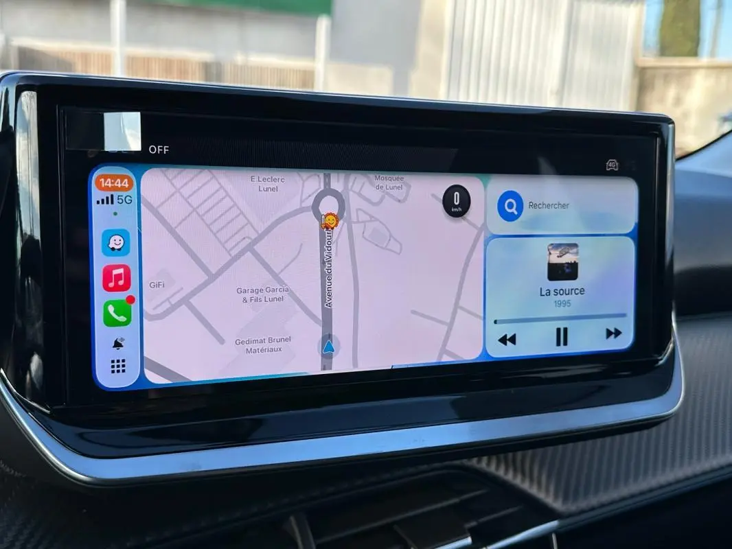 Écran tactile central affichant la navigation et la musique dans l’habitacle d’une Peugeot 208 blanc, version Hybrid 110 e-DCS6 Allure.