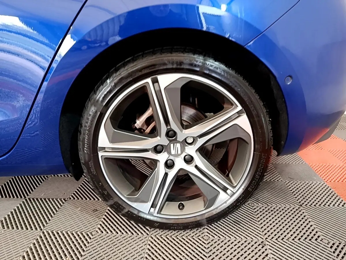 Gros plan sur la roue arrière droite d’une SEAT Leon bleu 2021 avec jante alliage cinq branches bicolore.
