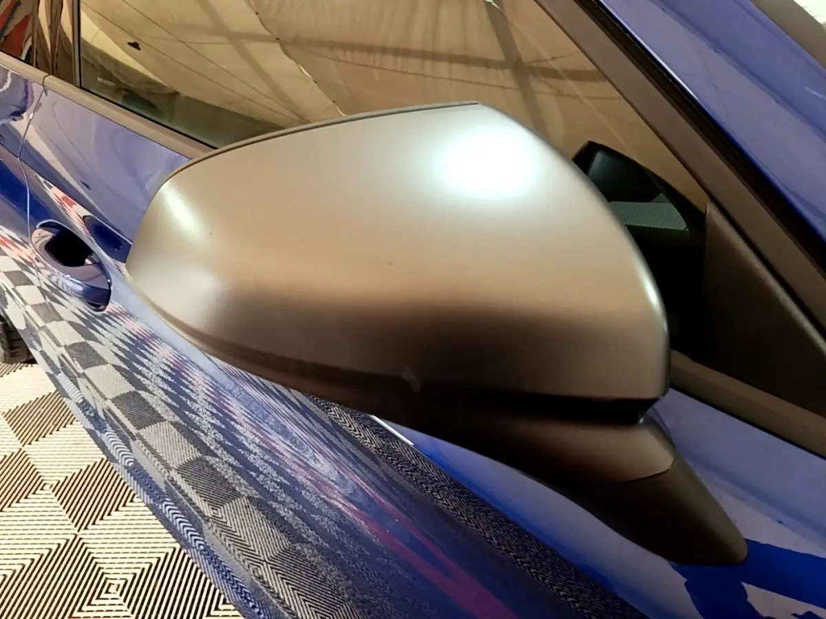 Rétroviseur côté gauche argenté sur SEAT Leon bleu, vue rapprochée du côté conducteur avec reflet au sol.