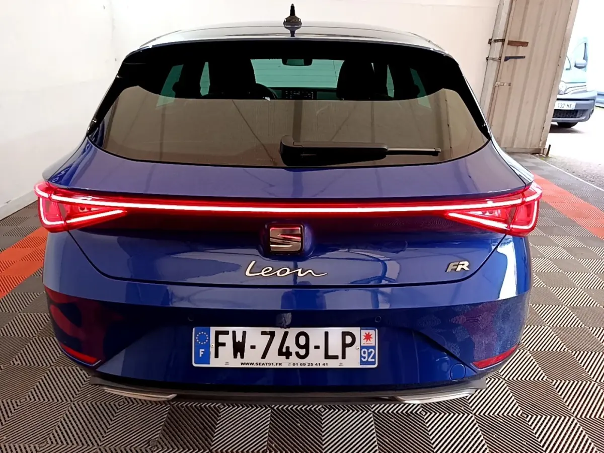 Vue arrière d'une SEAT Leon FR bleu avec feux arrière LED en bandeau lumineux allumé dans un garage.
