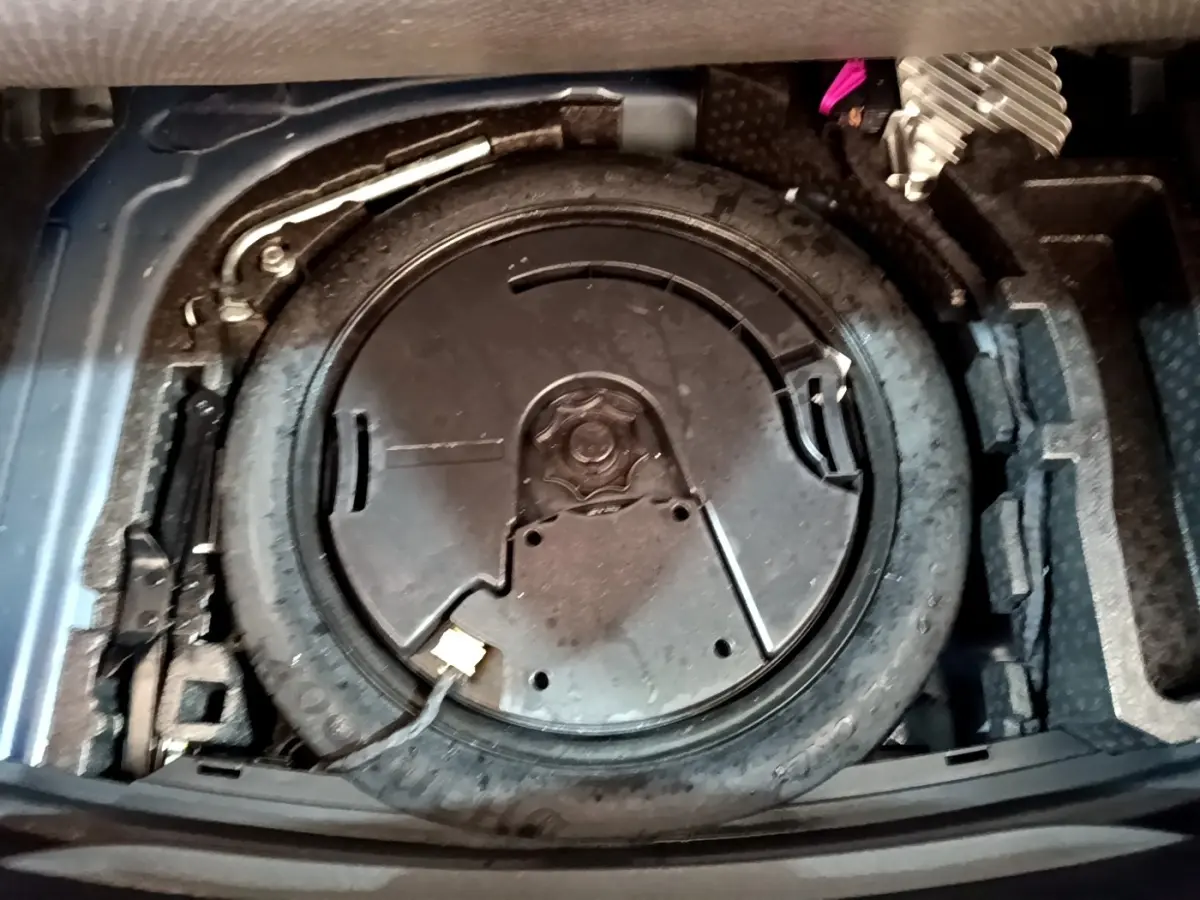 Vue en plongée sur la roue de secours et le kit de réparation dans le coffre d'une SEAT Leon 1.5 eTSI bleu 2021.