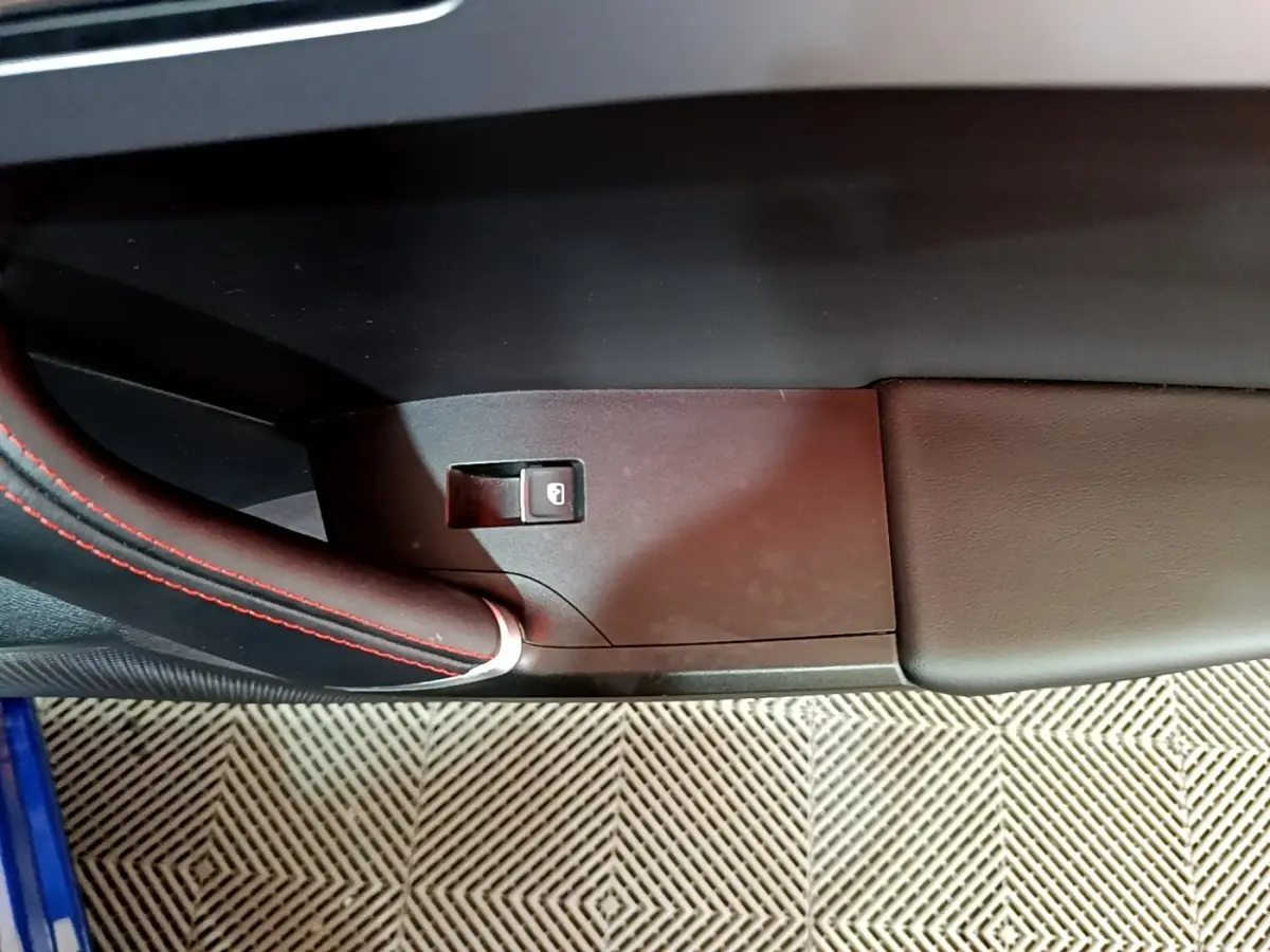 Détail de la poignée intérieure côté gauche avec surpiqûres rouges sur une SEAT Leon bleu 2021.