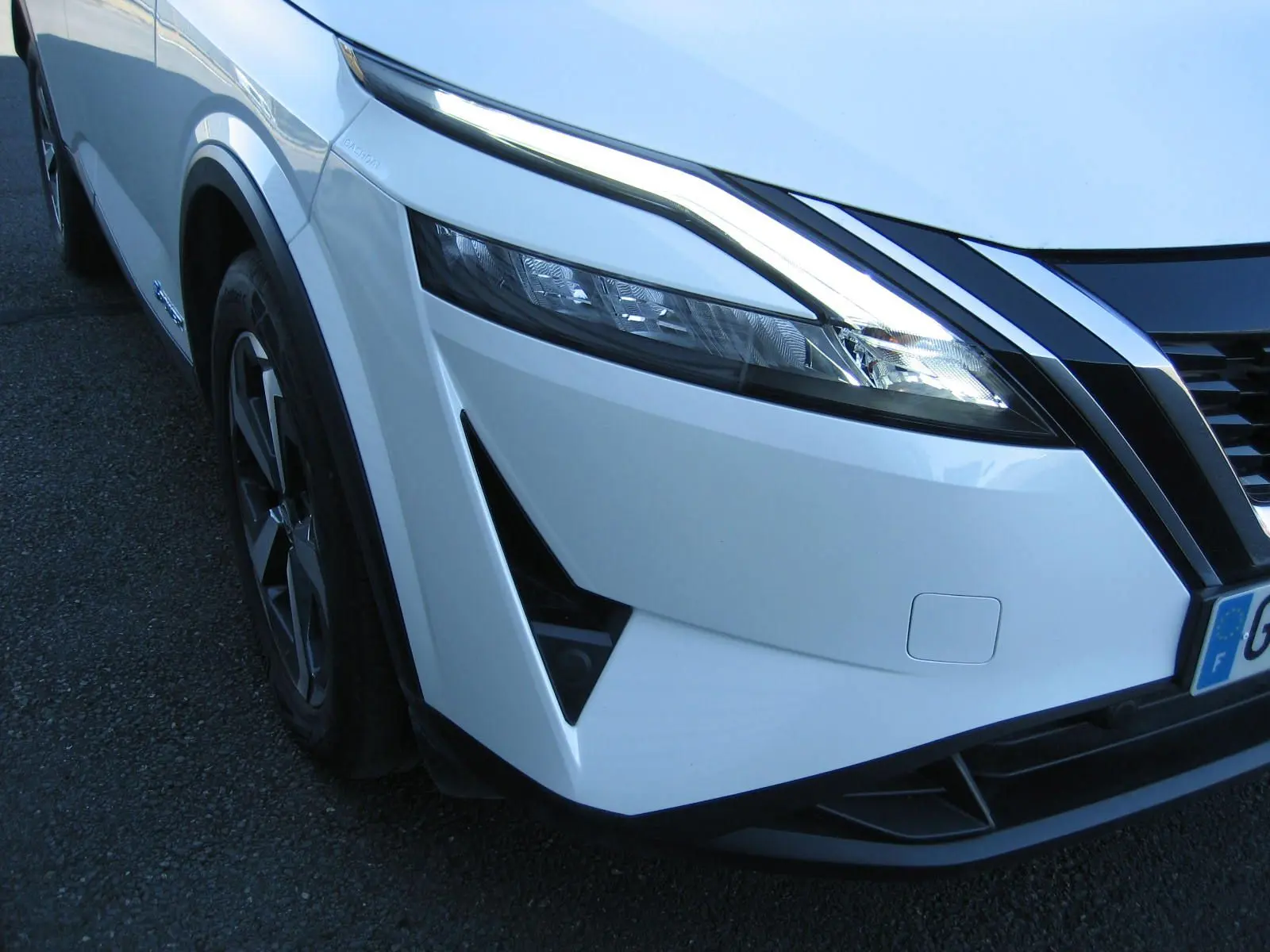 Vue 3/4 avant droit du Nissan Qashqai blanc nacré, mettant en valeur son phare LED et la calandre noire distinctive.