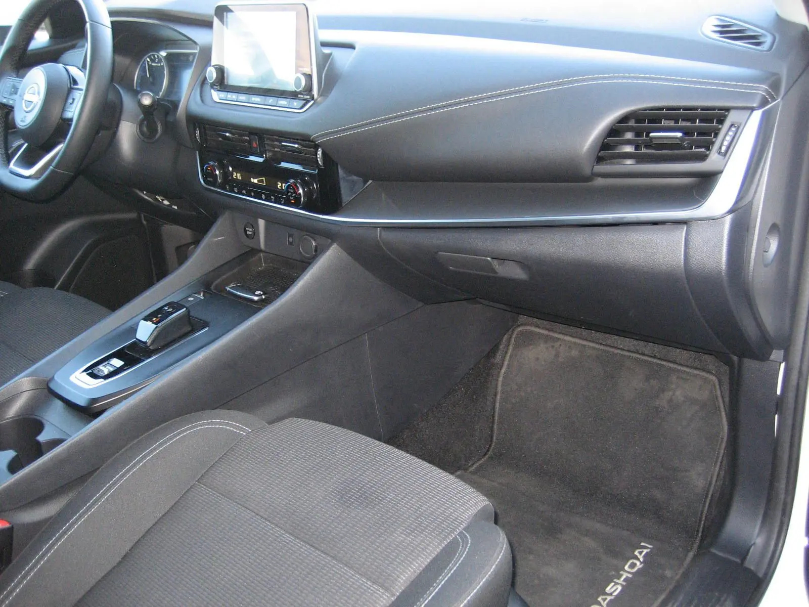 Vue intérieure côté passager du Nissan Qashqai 2024, montrant la console centrale et le tapis avec logo Qashqai.