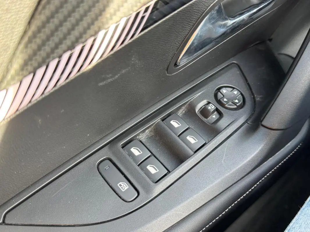 Gros plan sur les commandes des vitres électriques et rétroviseurs sur la porte côté conducteur du Peugeot 2008 noir.