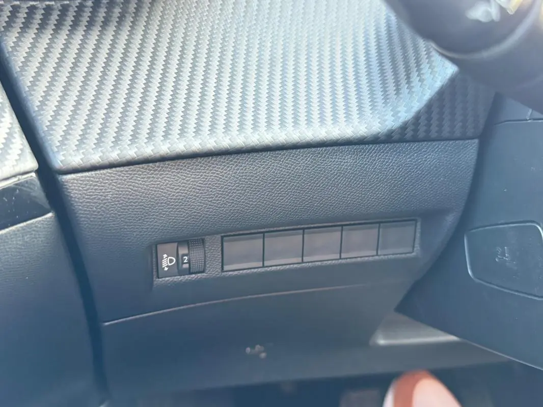 Détail intérieur montrant la console côté conducteur avec finition carbone et commandes d’éclairage du Peugeot 2008 noir.