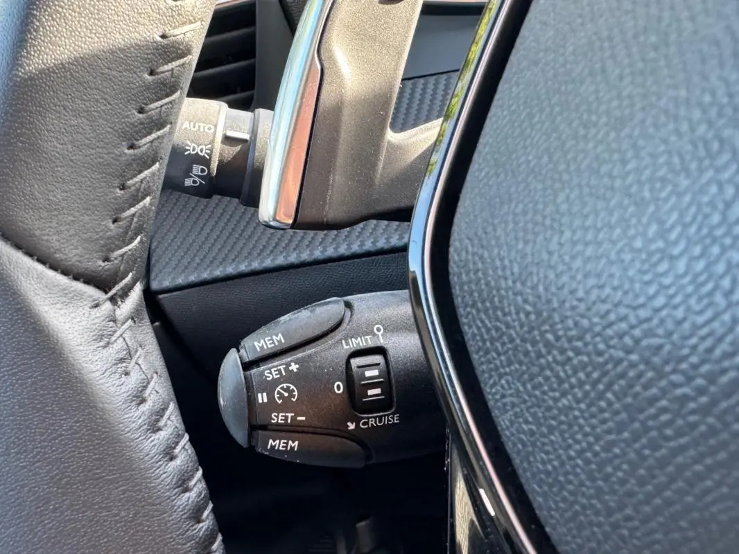 Gros plan sur la commande de régulateur de vitesse au volant d’un Peugeot 2008 noir Hybrid 136 e-DCS6 Allure.