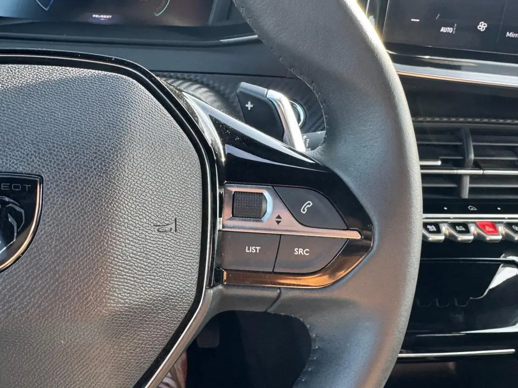 Gros plan sur le volant noir du Peugeot 2008 Hybrid 136 Allure 2025, avec commandes intégrées et tableau de bord partiel visible.