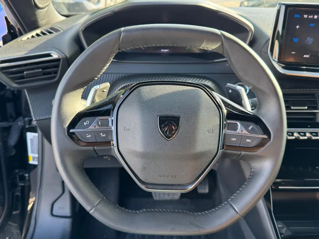 Vue rapprochée du volant noir de la Peugeot 2008 Hybrid 136 e-DCS6 Allure avec commandes intégrées.