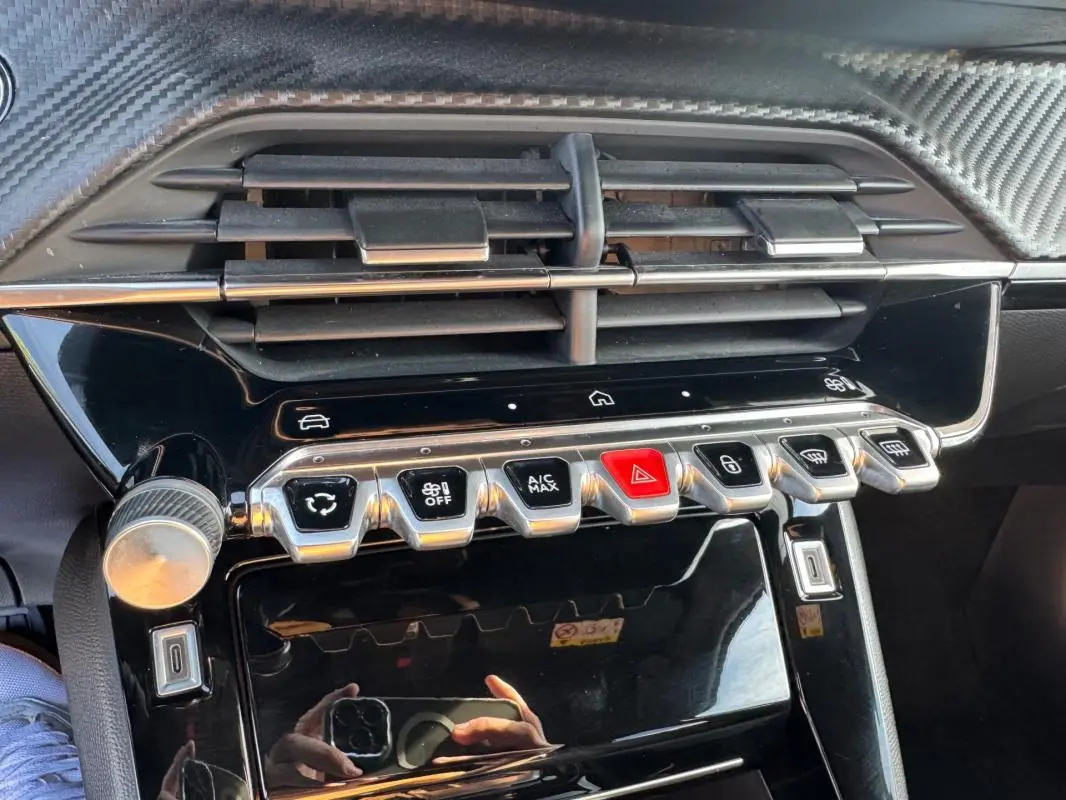 Gros plan sur la console centrale noire du Peugeot 2008 Hybrid 136, avec boutons de commande et aérateurs.