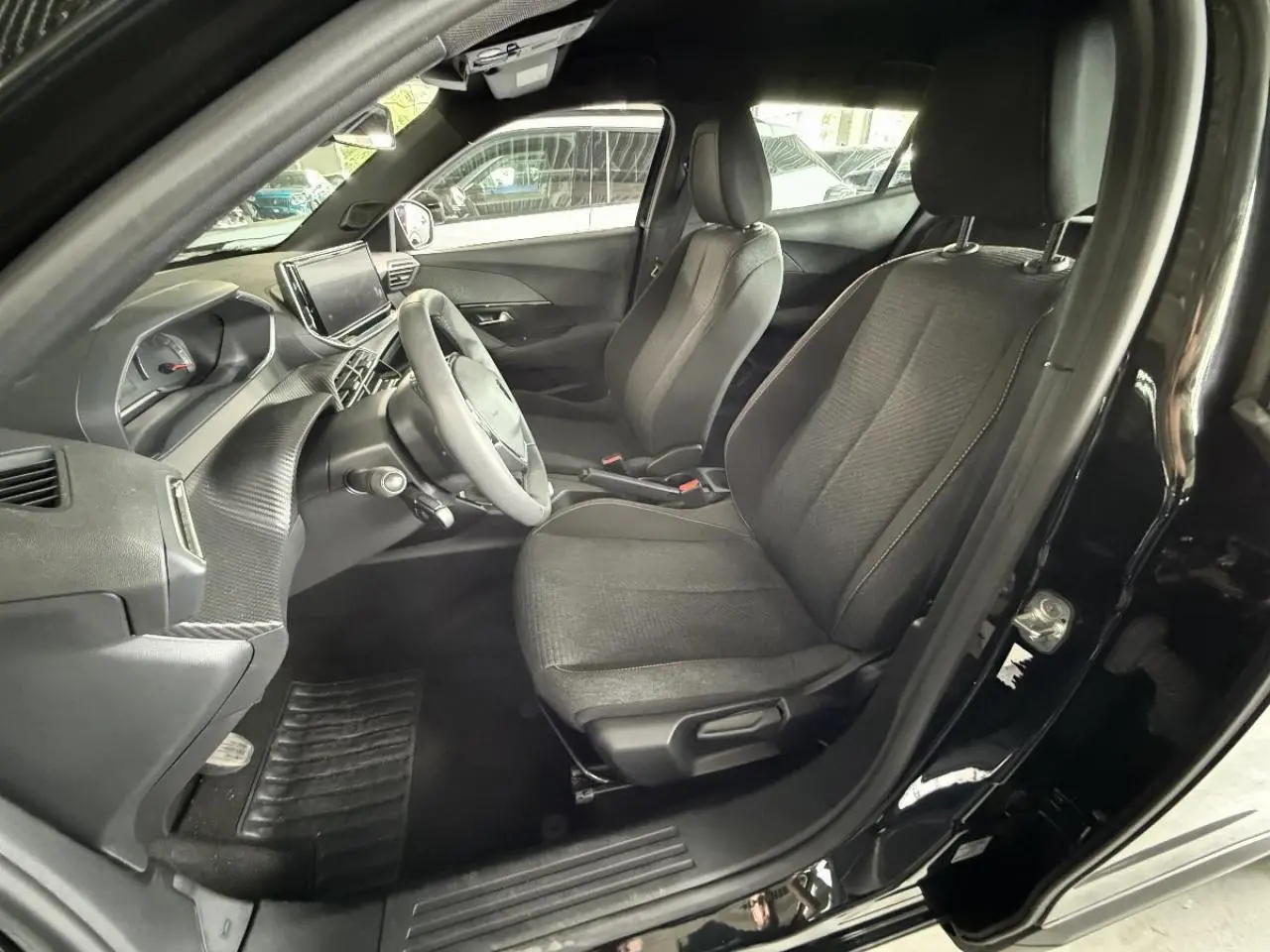 Intérieur avant droit du Peugeot 2008 2024 essence blanc okenite, sièges tissu noirs et tableau de bord moderne.