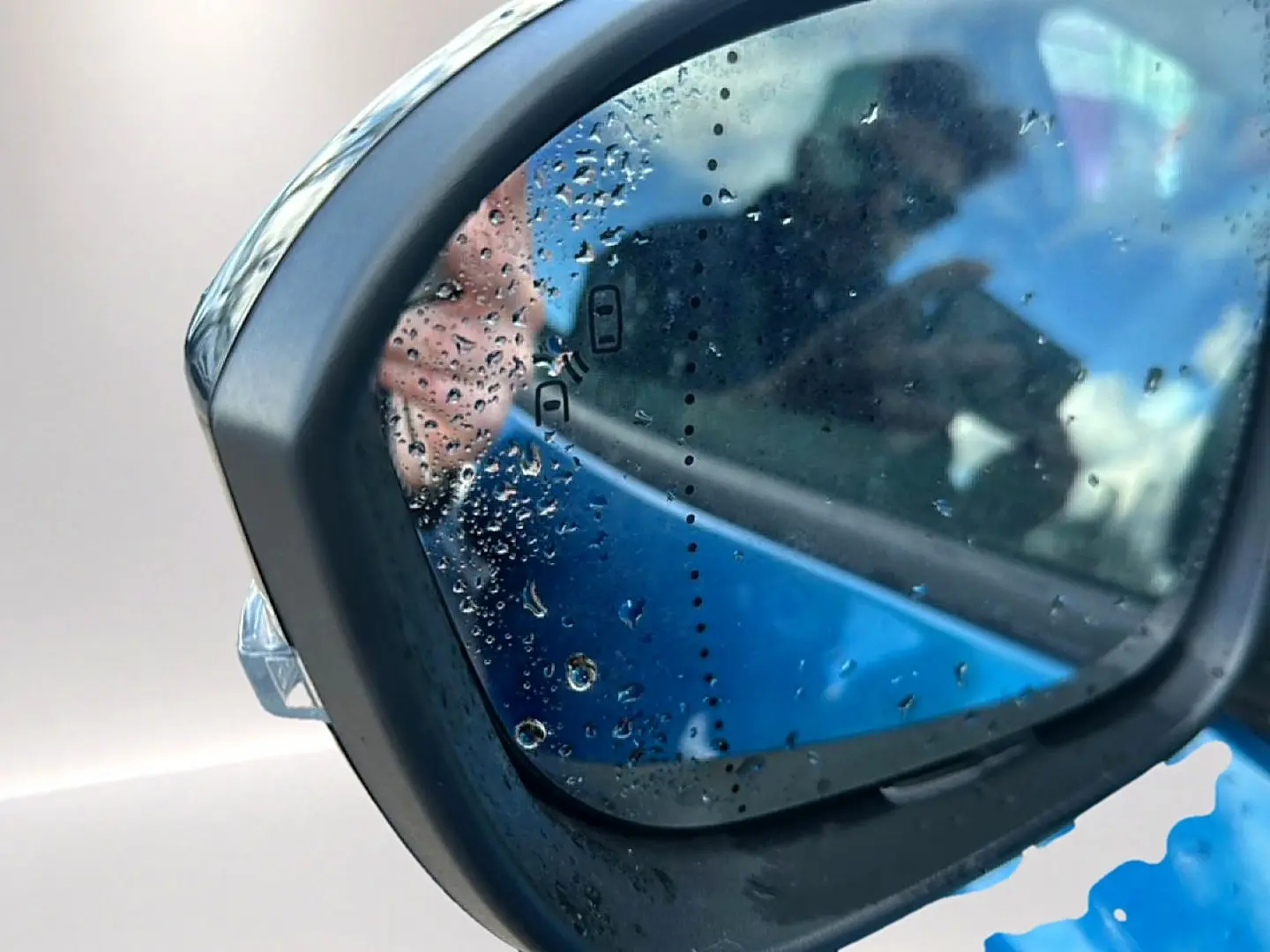 Rétroviseur extérieur gauche bleu outremer de Renault Austral 2026 avec gouttes d'eau et reflet flou.