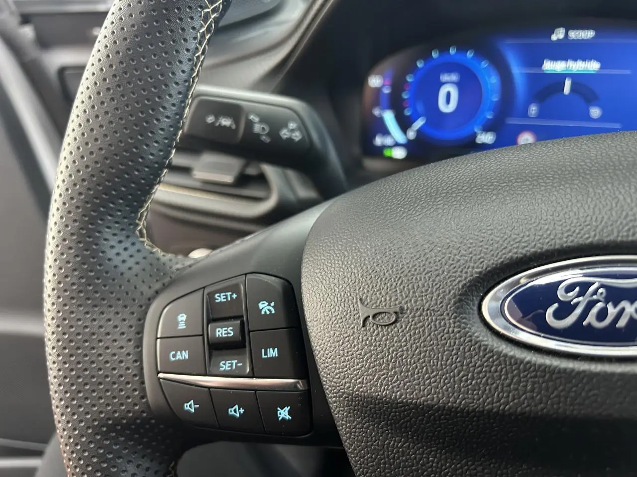 Gros plan sur le volant perforé noir du Ford Puma avec commandes intégrées et tableau de bord numérique bleu en arrière-plan.