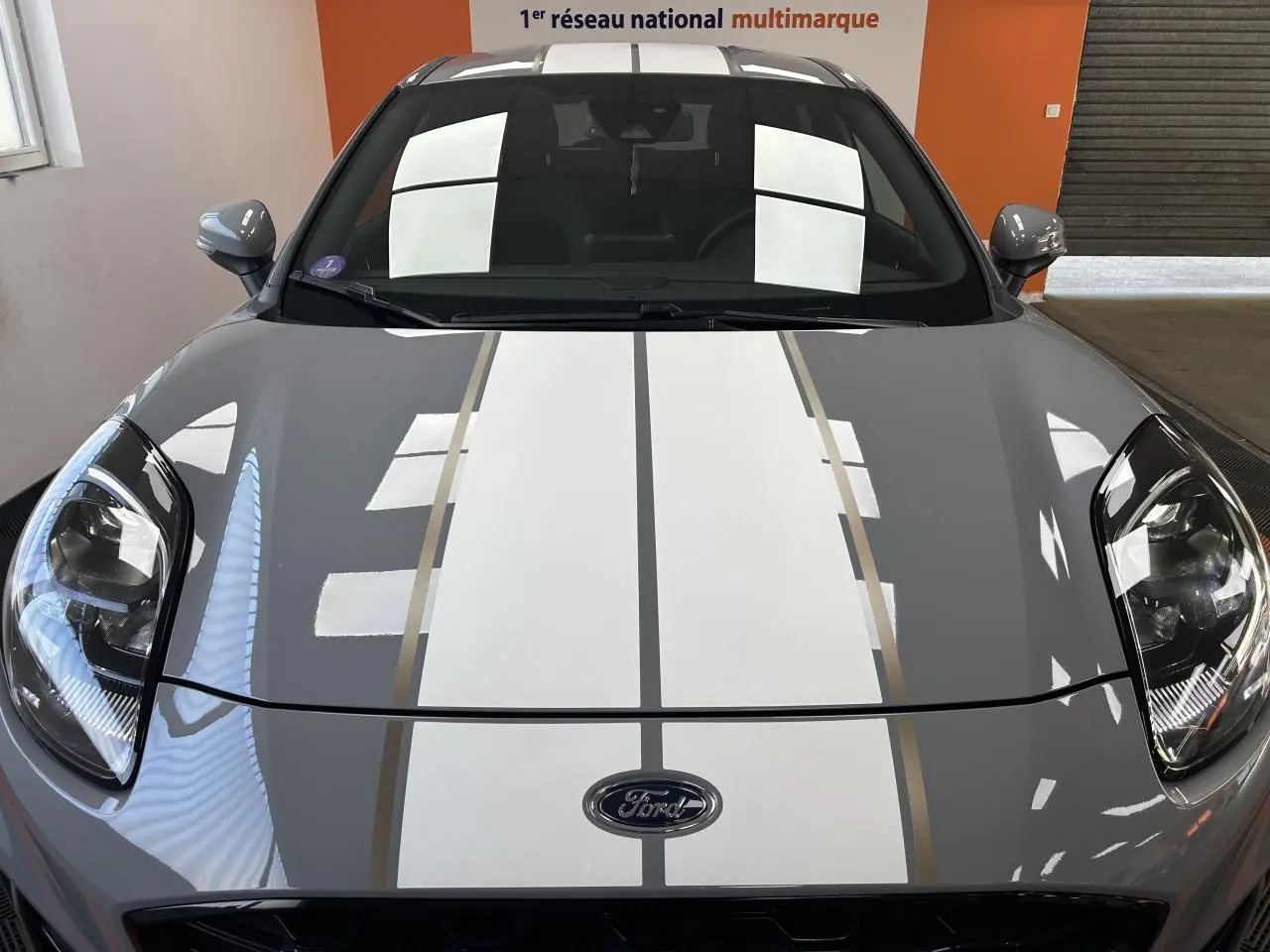 Vue avant rapprochée du Ford Puma gris avec bandes blanches et jantes ST Line Gold visibles en reflet.