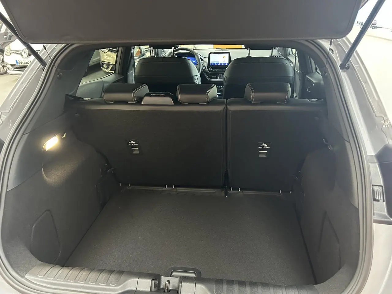 Coffre ouvert d'un Ford Puma gris 3/4 arrière, montrant l'espace de chargement et les sièges arrière noirs.