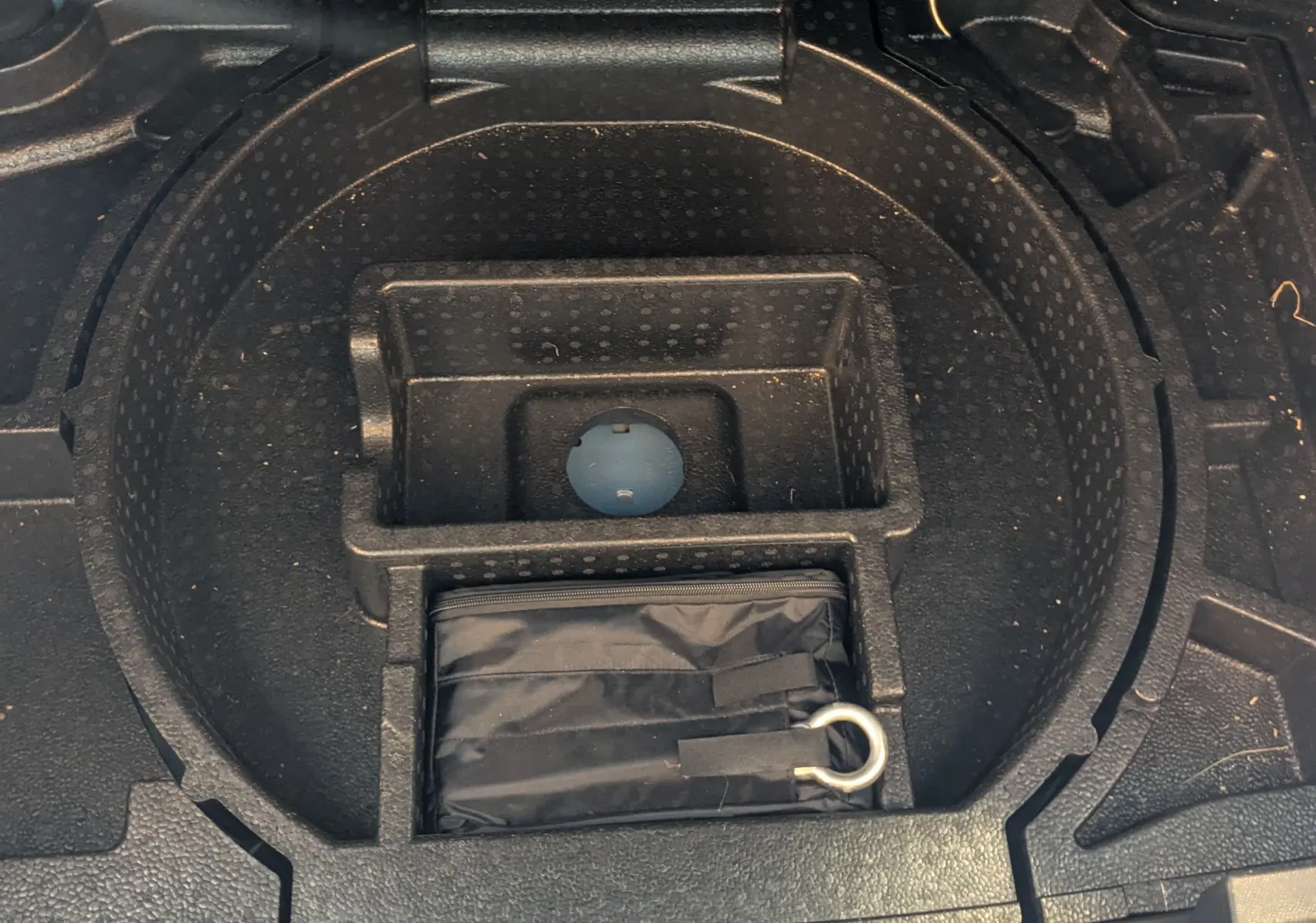 Coffre ouvert d'une Opel Astra bleu 2022, vue sur le rangement sous le plancher avec kit de secours noir.