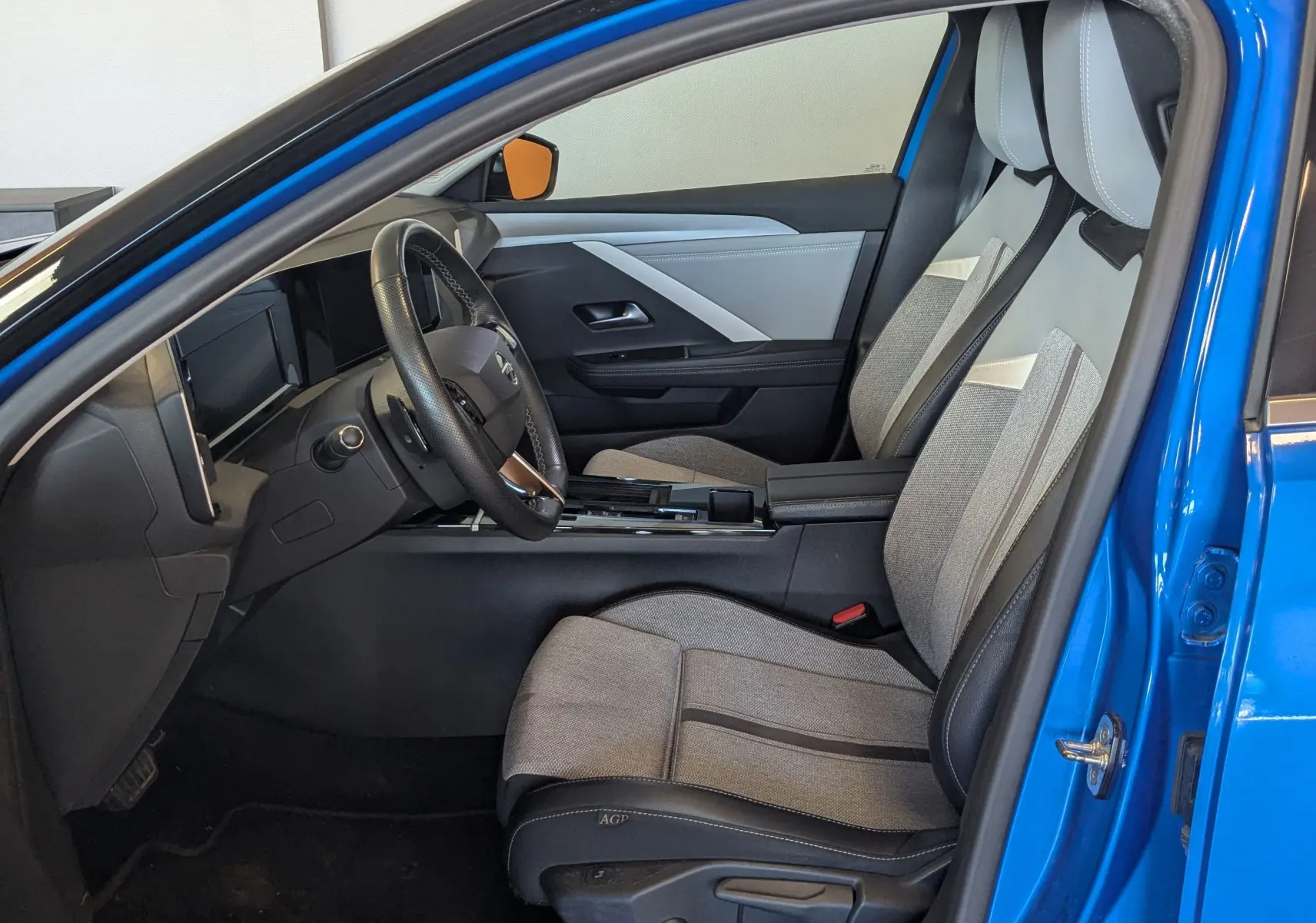Intérieur côté conducteur d'une Opel Astra bleu 2022, sièges bi-matière gris et noir avec tableau de bord moderne.