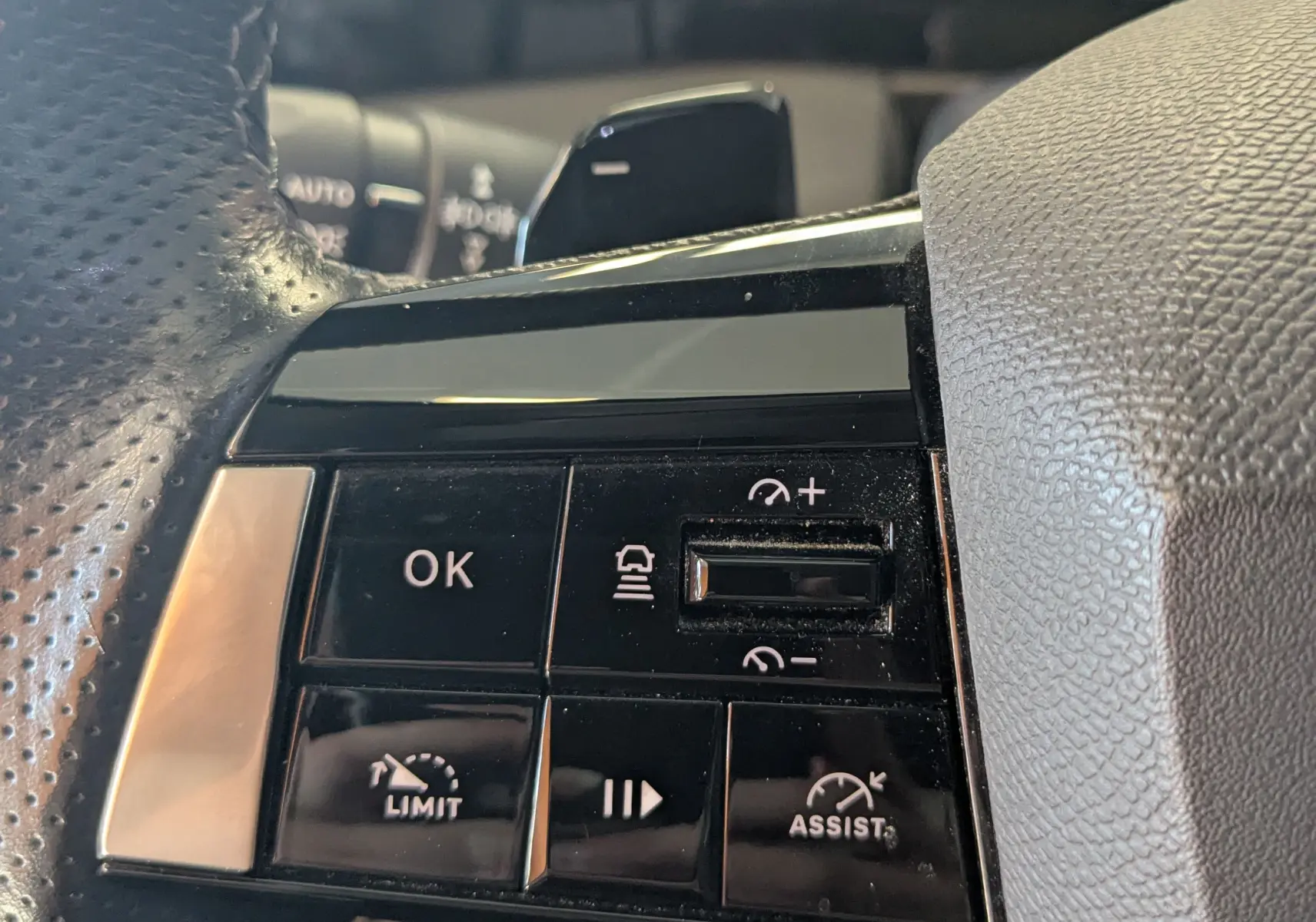 Gros plan sur les commandes noires du volant perforé côté gauche de l'Opel Astra 2022 bleu, avec boutons de régulateur et assistant.