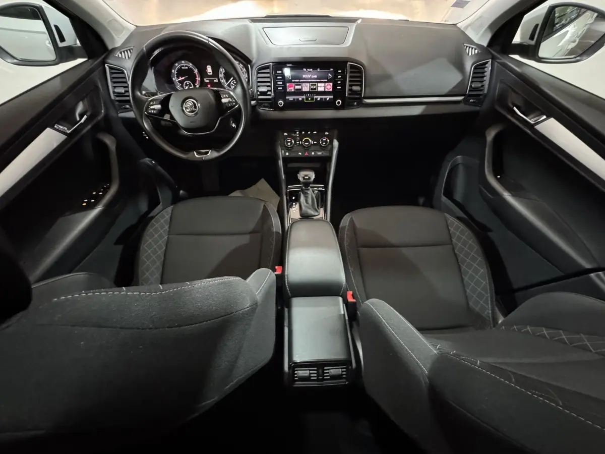 Vue intérieure avant du Skoda Karoq 1.5 TSI blanc, tableau de bord moderne avec écran tactile et volant multifonctions cuir.