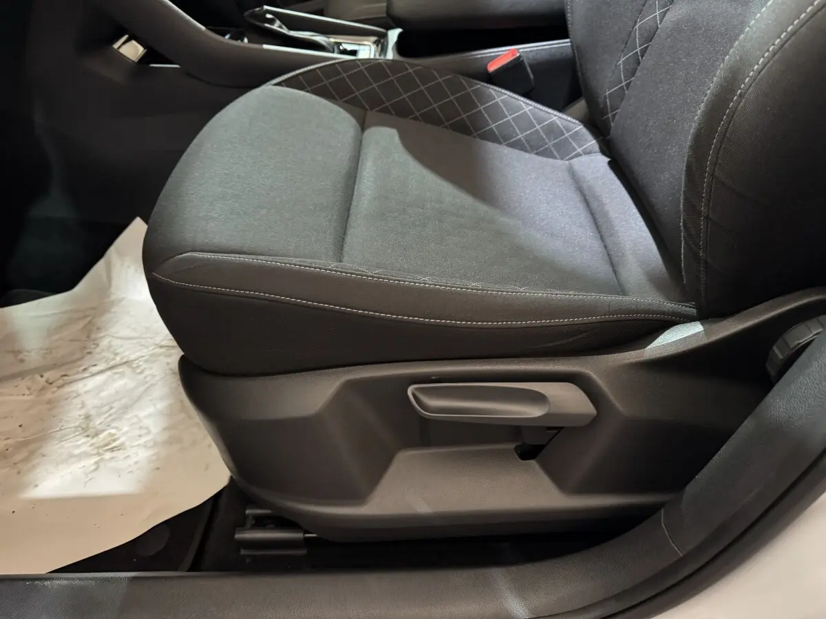 Gros plan sur le siège avant gauche gris foncé du Skoda Karoq blanc, montrant la manette de réglage latérale.