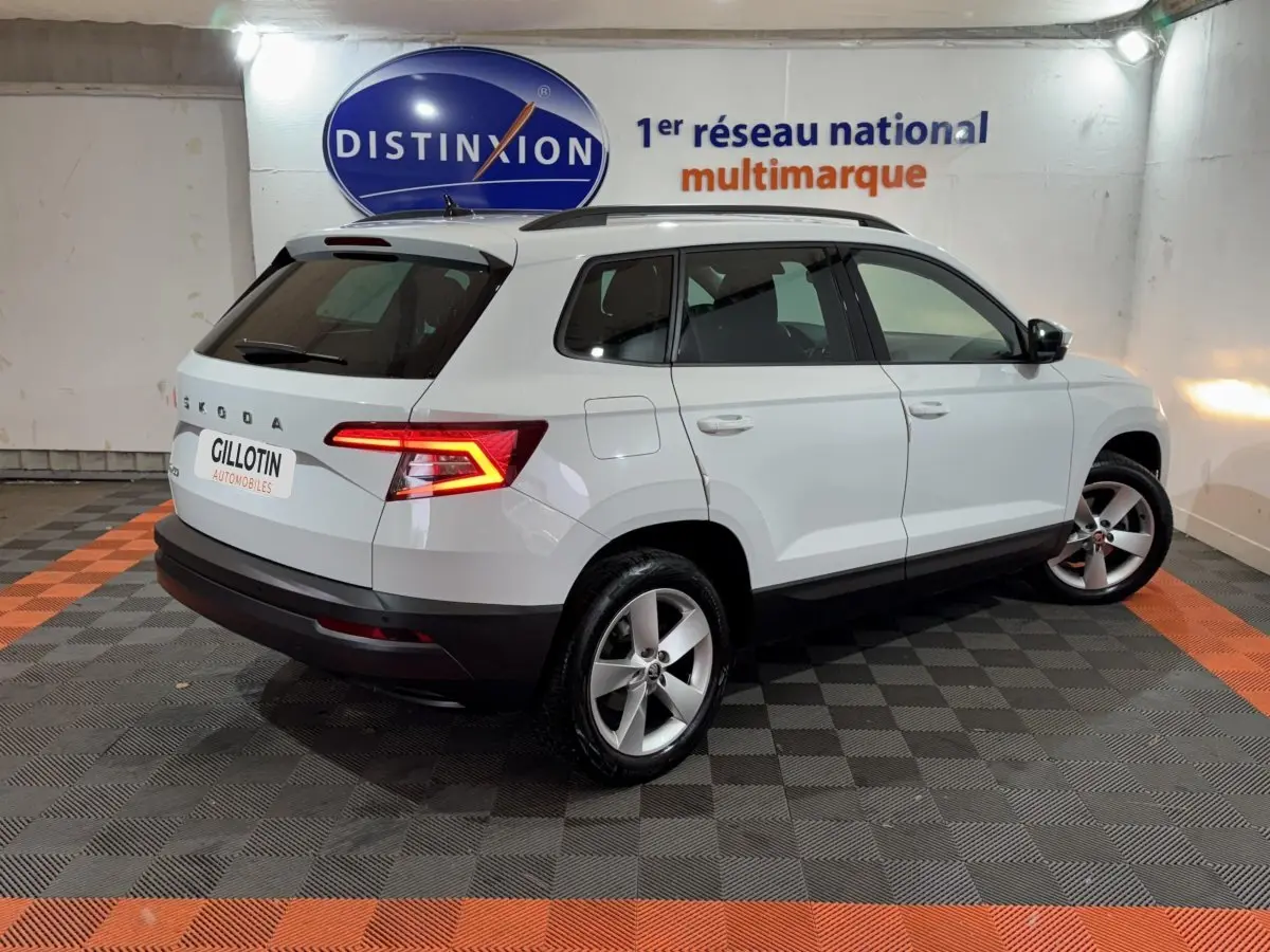 Vue 3/4 arrière droite d'un SUV SKODA KAROQ blanc avec feux arrière LED allumés dans un showroom.