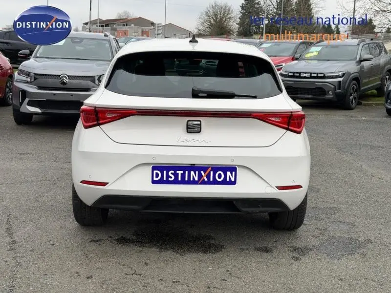 Vue arrière d'une SEAT Leon blanche 2025, soulignant la signature lumineuse rouge continue et le logo central.